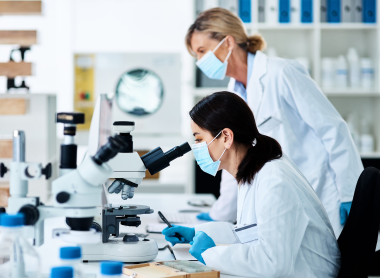 Scientists in a laboratory wearing protective masks, analyzing samples under a microscope.